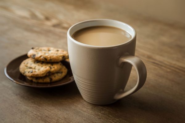 Cup of coffee with milk and cookies with chocolate pieces on the brown wooden table. Resting and enjoying time with coffee and sweets. Drink and snack concept.